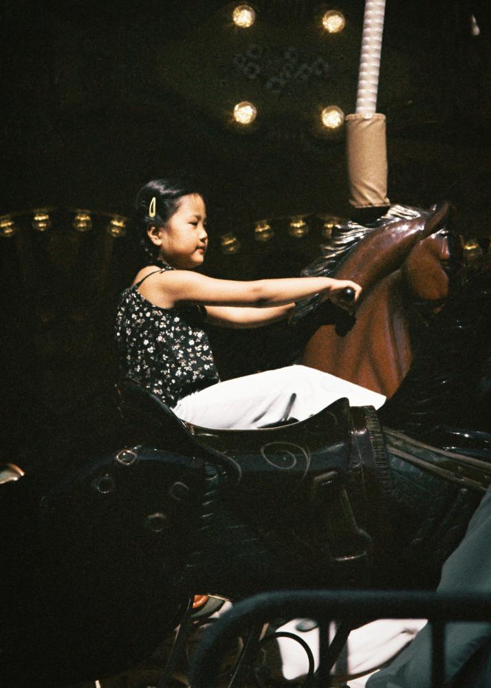 Ein junges Mädchen fährt auf einem Steckenpferd eines Karussells.