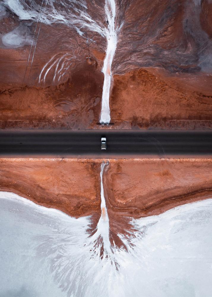 ine Straße, die durch eine surreal aussehende Landschaft mit roten und weißen Salzablagerungen führt.