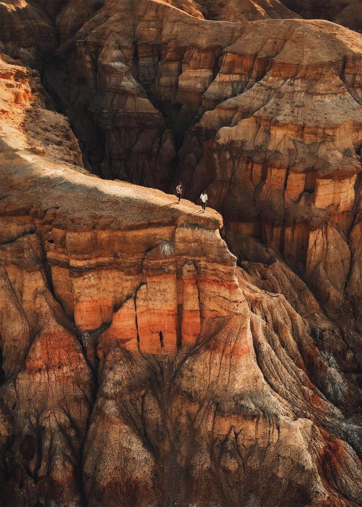 Zwei Personen stehen auf einem Felsvorsprung in einer trockenen, felsigen Landschaft und blicken in die Weite.