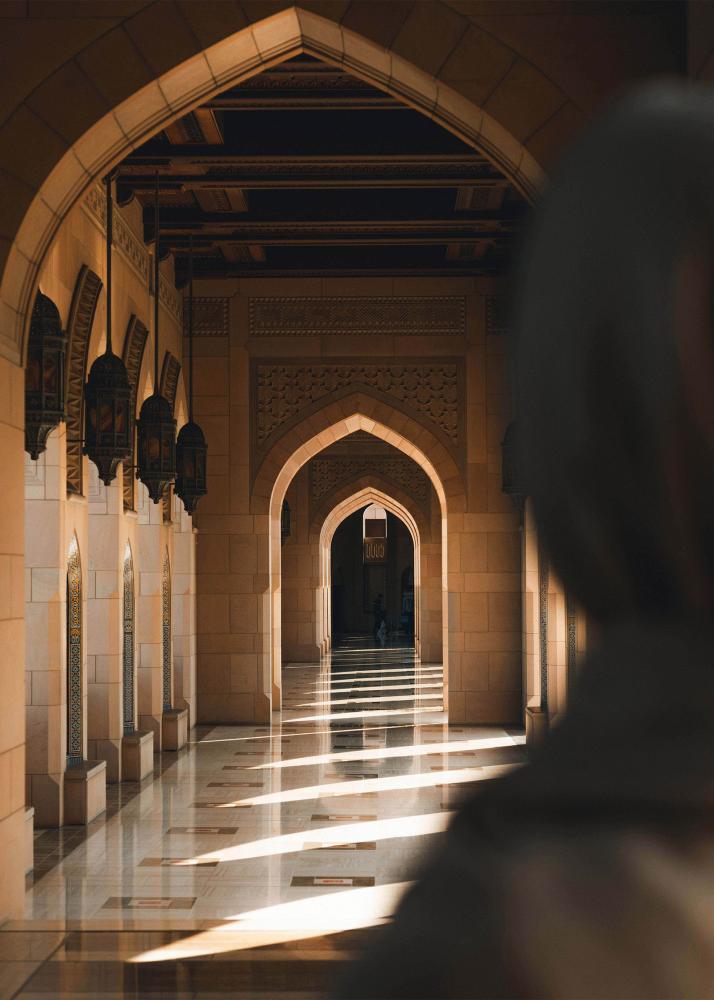 Ein langer, von Säulen gesäumter Korridor mit hohen Bögen und Laternen, der in einen hell erleuchteten Innenhof führt.
