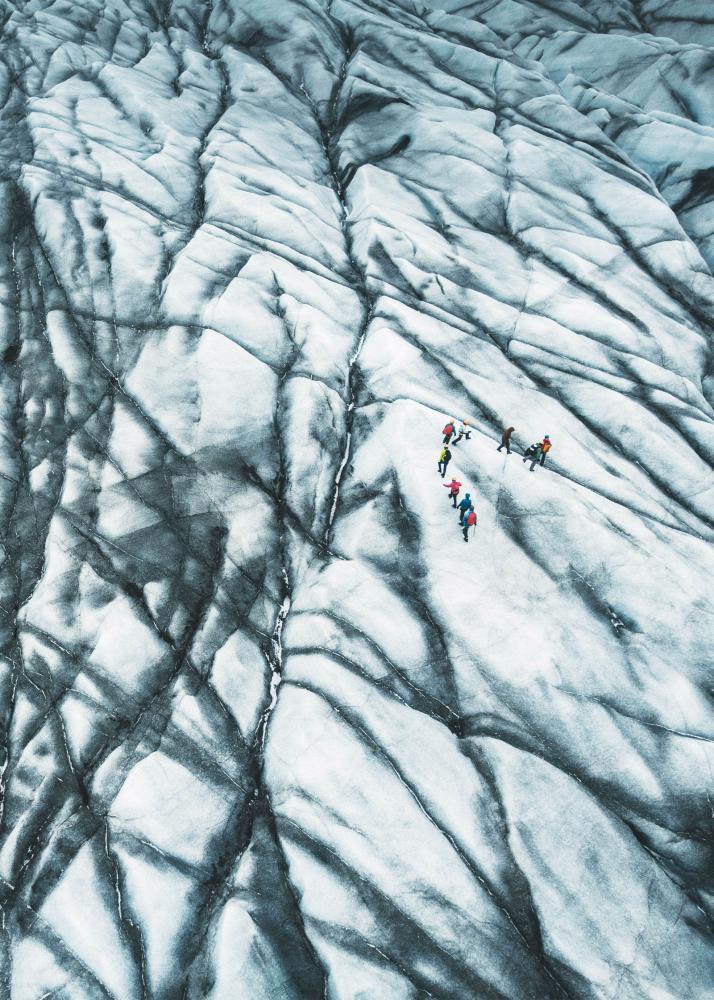 Eine Gruppe von Wanderern, die über ein gefrorenes Gletscherfeld mit tiefen Spalten und Rissen wandern.