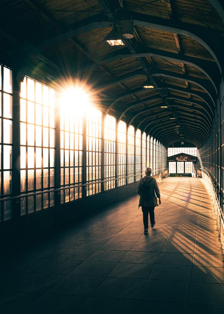 Eine Person geht durch einen beleuchteten, überdachten Korridor mit großen Fenstern.