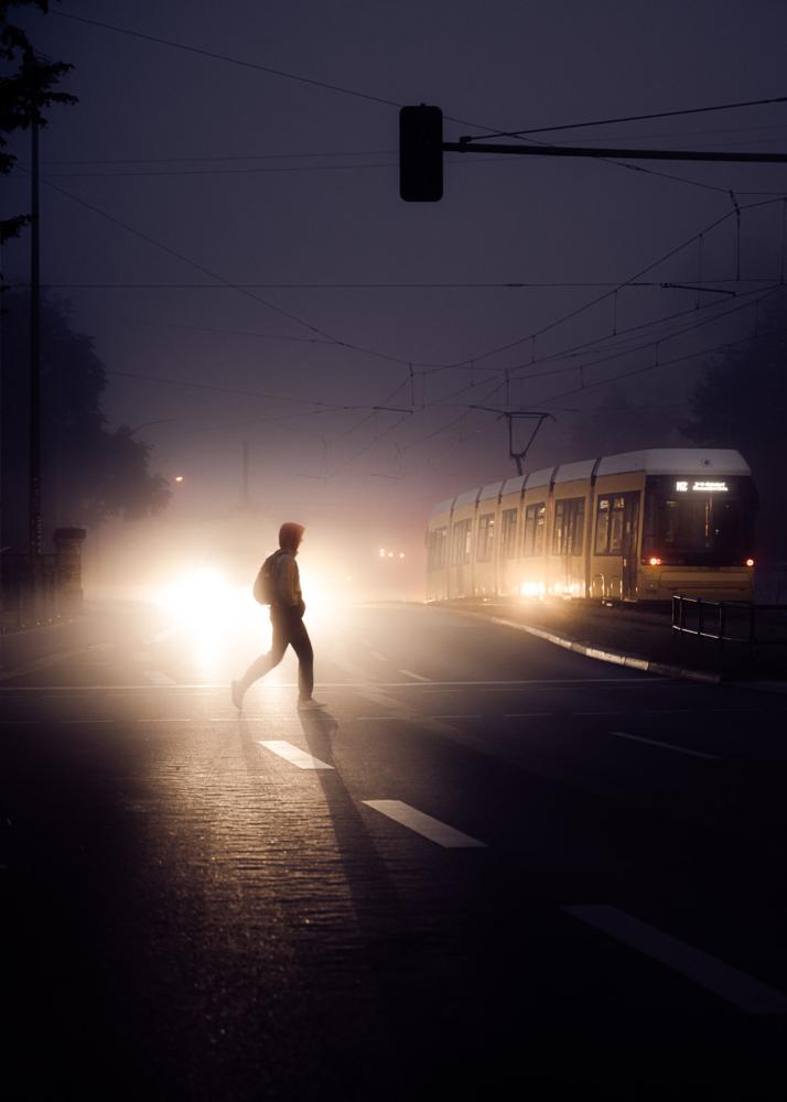 Eine Person überquert bei Nebel eine Straße, während eine Straßenbahn im Hintergrund zu sehen ist.