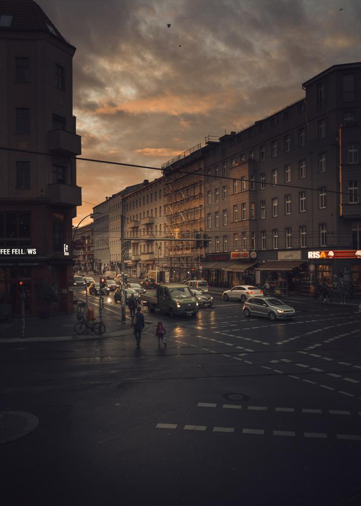 Eine belebte Kreuzung bei Sonnenuntergang mit mehreren Fahrzeugen und Fußgängern.