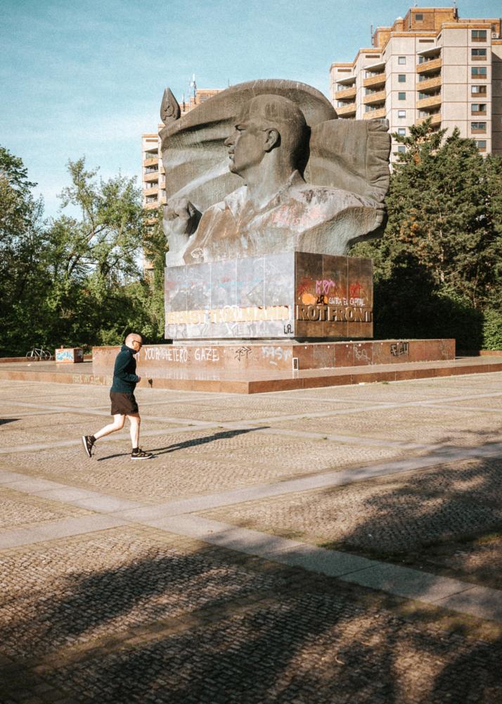 Ein Mann joggt vor einem großen Denkmal mit einem Hochhaus im Hintergrund.