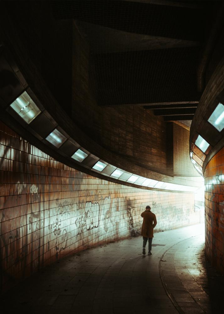 Eine Person steht in einem beleuchteten Tunnel mit Graffiti an den Wänden und hält ein Fahrrad.