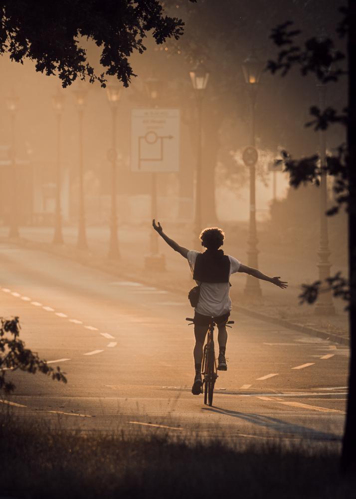 Ein Radfahrer fährt mit ausgebreiteten Armen durch den Morgennebel auf einer leeren Straße.