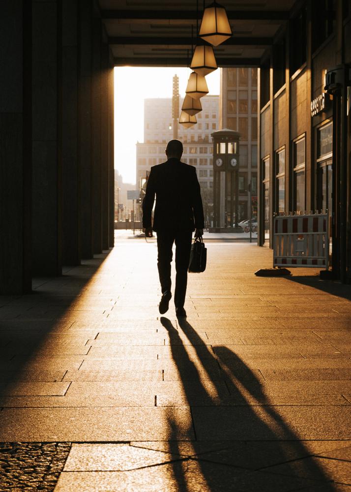 Ein Mann in einem Anzug geht durch einen beleuchteten Korridor mit Säulen und trägt eine Aktentasche.
