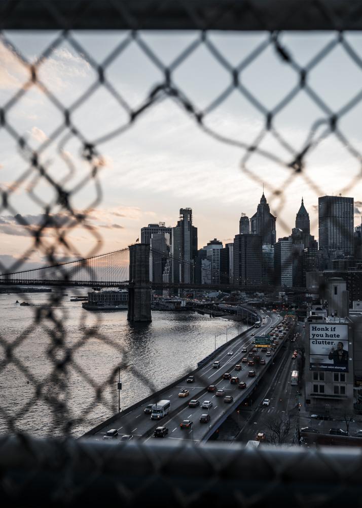 Eine Stadtansicht durch einen Zaun, mit einer Brücke und Hochhäusern im Hintergrund.