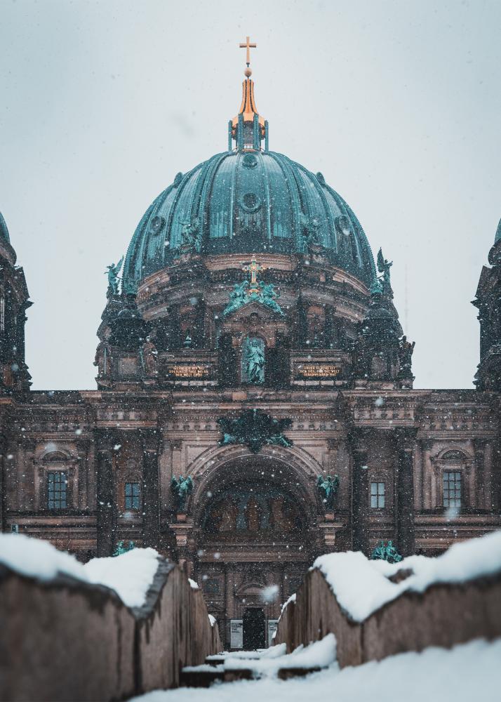 Ein historisches Gebäude mit einer grünen Kuppel, bedeckt mit Schnee, in einer winterlichen Umgebung.