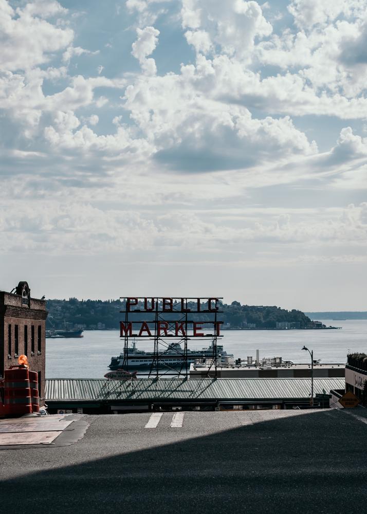 Ein Schild mit der Aufschrift 'Public Market' am Wasser, mit Booten und einer Stadtlandschaft im Hintergrund.