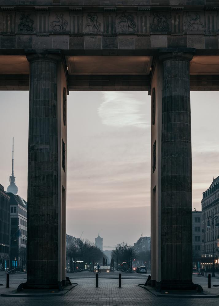 Blick durch das Brandenburgertor, das den Blick auf eine Stadtstraße mit dem Fernsehturm im Hintergrund freigibt.