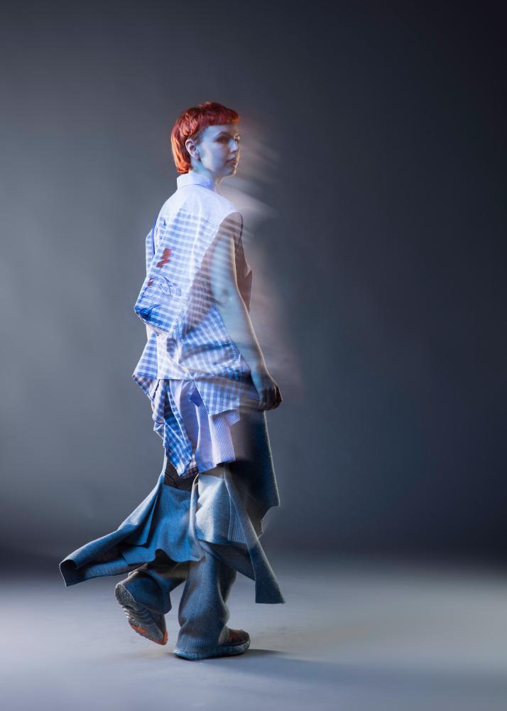 Eine Person mit rotem Haar in einem gestreiften Hemd und weiten Hosen, fotografiert mit Bewegungseffekten.