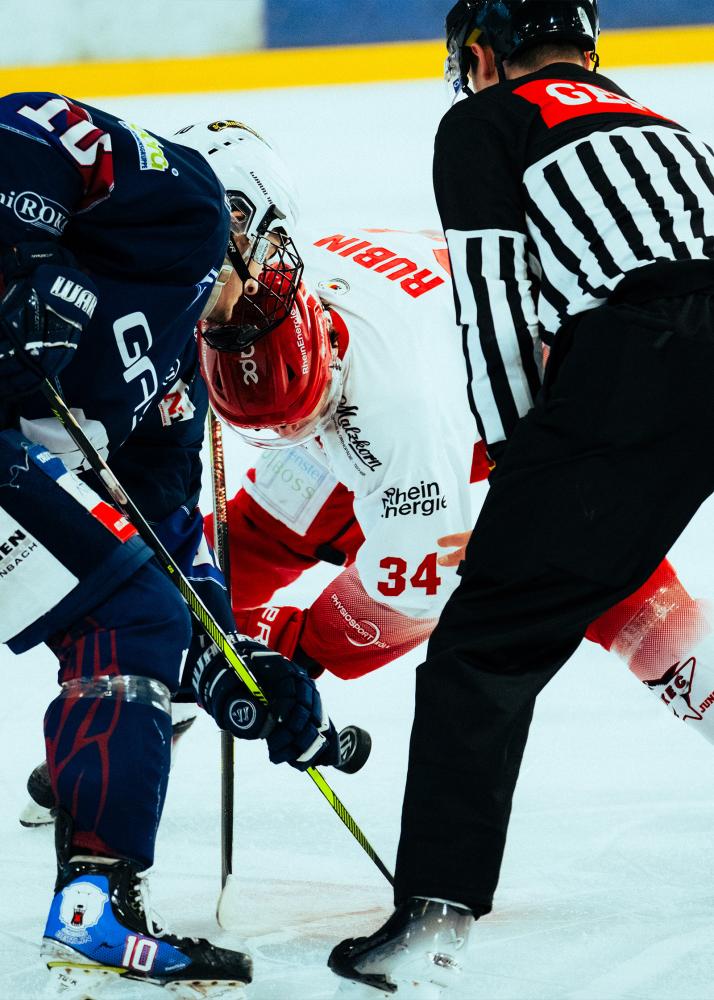 Zwei Eishockeyspieler kämpfen um den Puck. Ein Schiedsrichter beobachtet das ganze.