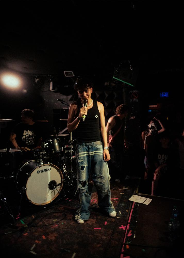 Ein junger Musiker, eingerahmt durch Instrumente, steht auf einer Bühne und singt in sein Mikrofon.