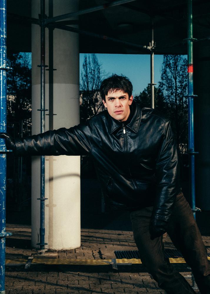 Ein Mann lehnt an einem Baugerüst und schaut grimmig in die Kamera.