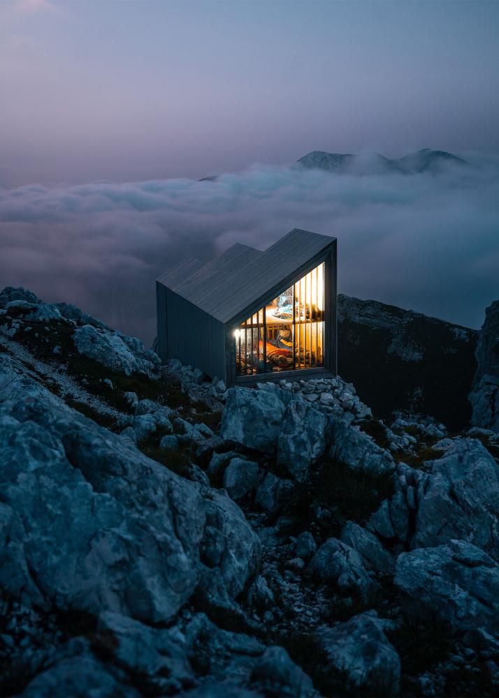 Ein modernes, minimalistisches Gebäude steht auf einem felsigen Gipfel mit Blick auf eine Wolkenlandschaft.