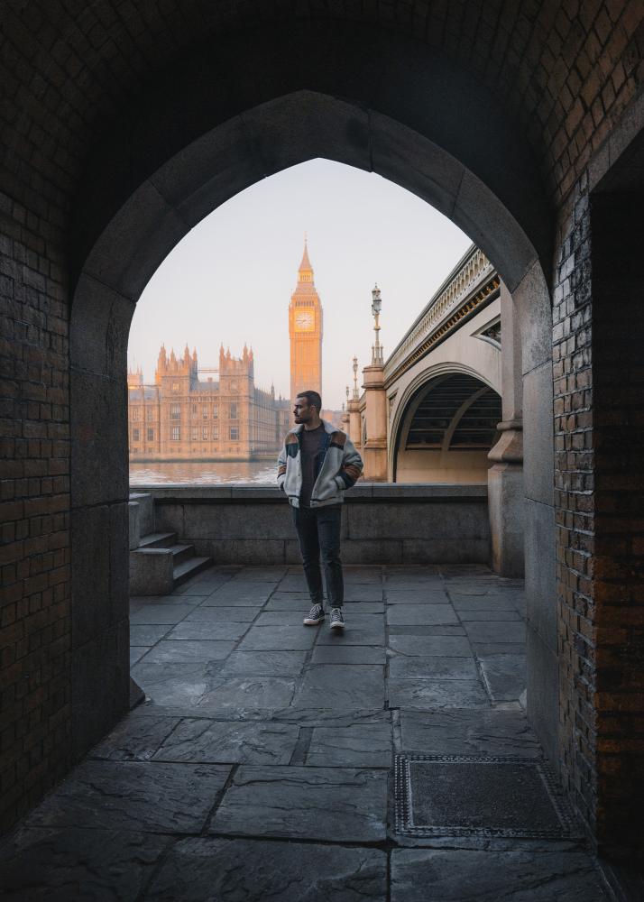 Ein Mann steht in einem Gewölbe mit Blick auf den Big Ben und ein historisches Gebäude am Flussufer.