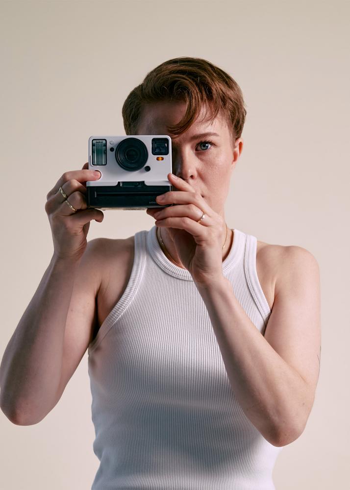 Eine Frau schaut durch eine Polaroid Kamera in die Kamera.