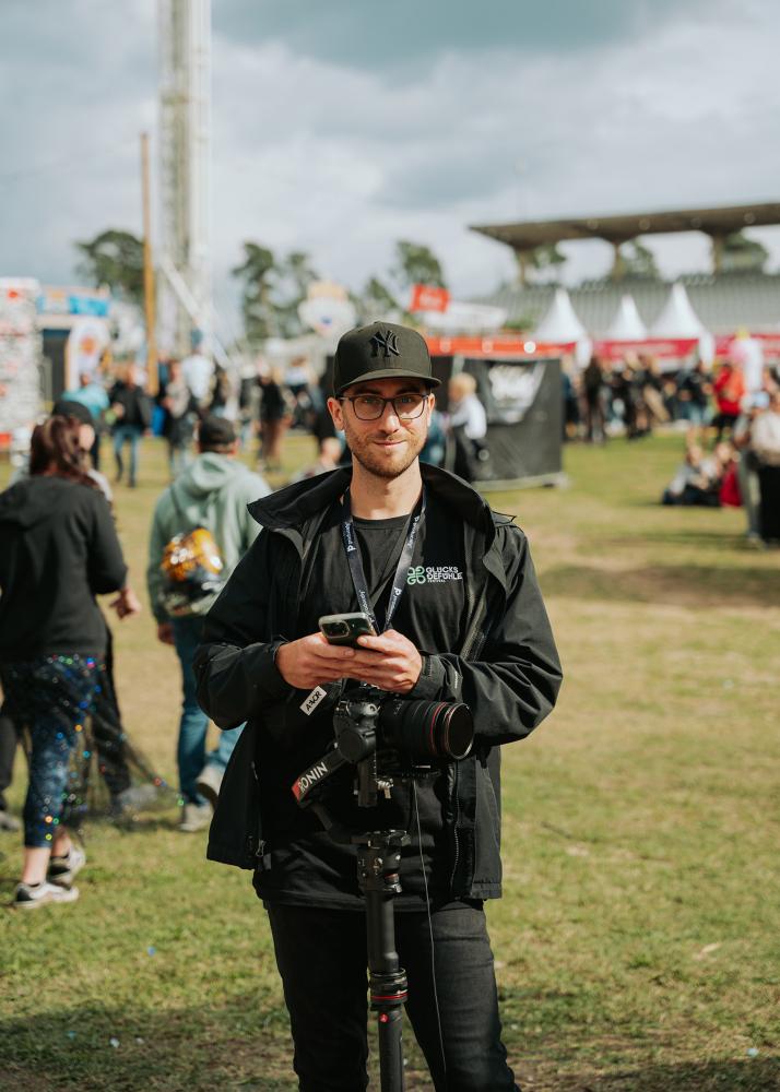 Der Fotograf Felix Noak auf einem Festival, der eine Kamera hält und in die Kamera lächelt.