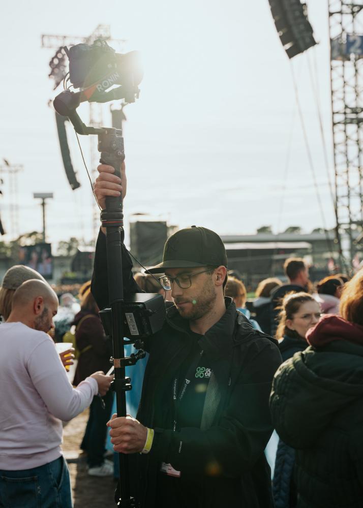 Der Fotograf Felix Noak auf einem Festival, der eine Kamera auf einem Stativ bedient, während die Sonne durch die Kamera scheint.