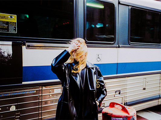 Eine Frau mit blonden Haaren und schwarzem Mantel steht vor einem Bus.