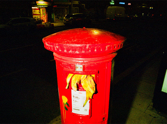 Ein roter Briefkasten mit einem Aufkleber und einer Bananenschale die heraus schaut.