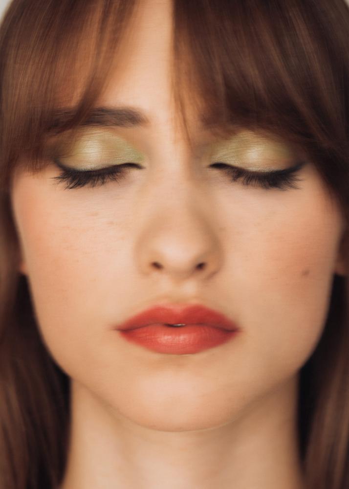 Ein Porträt einer Frau mit rotem Lippenstift und grünen Lidschatten, die die Augen geschlossen hat.