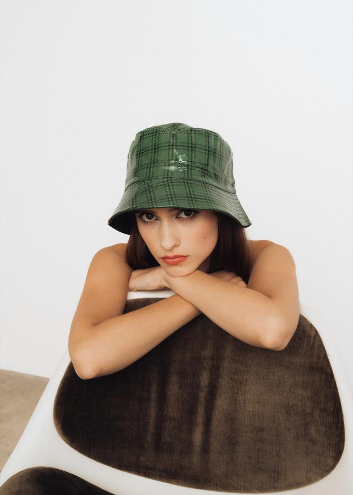 Eine Frau in einem grünen Hut lehnt sich auf einen braunen Stuhl.