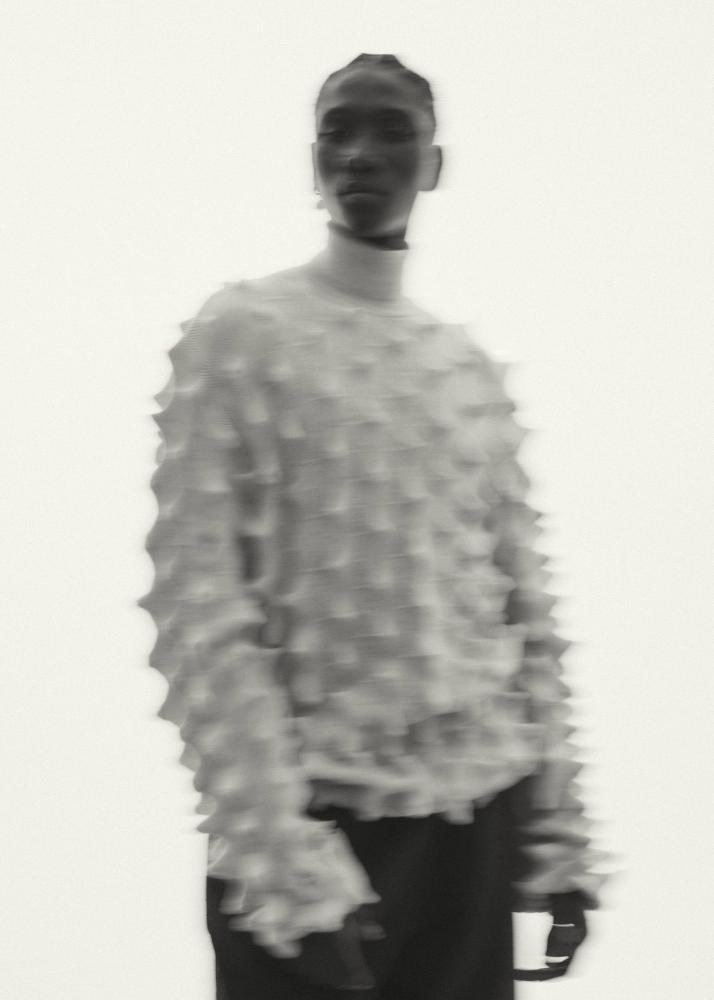 Ein Mann in einem strukturierten, weißen Pullover mit einem durch Bewegung verschwommenen Gesicht.