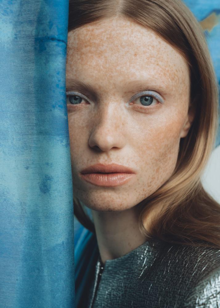 Eine Frau mit Sommersprossen schmiegt sich an ein blaues Tuch.