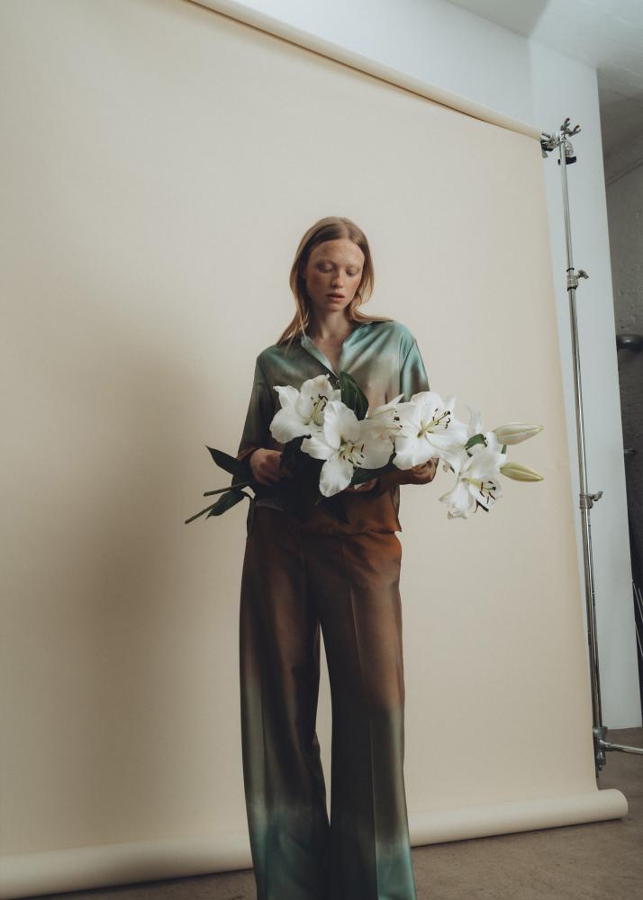 Eine Frau in einem grünen Oberteil und braunen Hosen hält einen Strauß weißer Blumen.