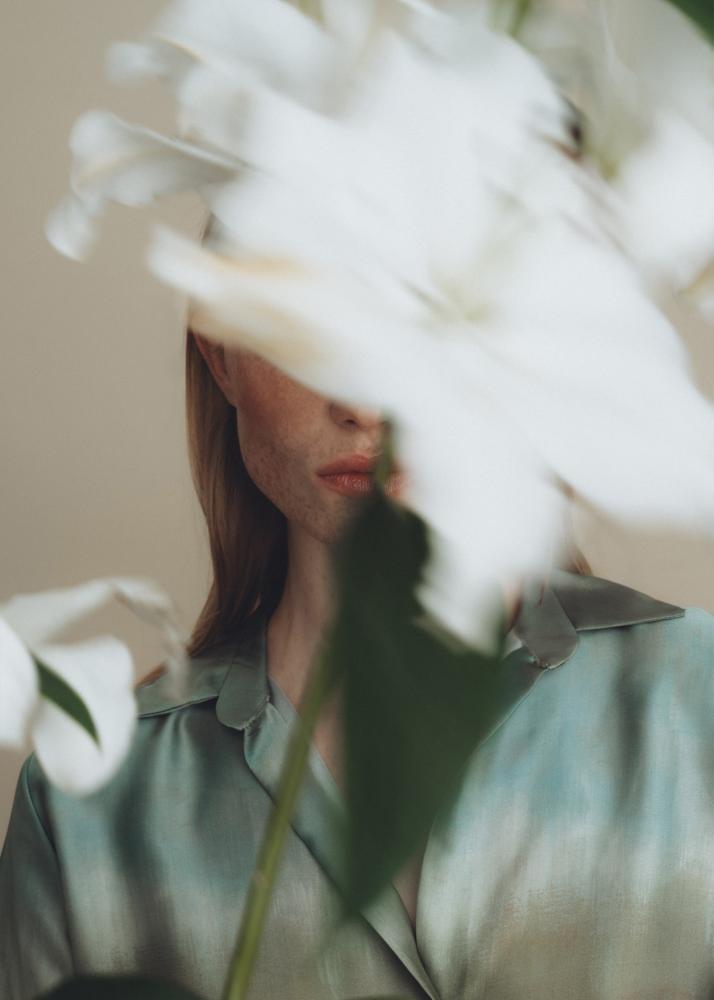 Eine Frau mit einer weißen Blume vor ihrem Gesicht, die ein grünes Oberteil trägt.