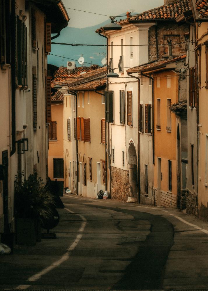 Eine enge Gasse mit alten Gebäuden und geschlossenen Läden, die von der Sonne beleuchtet wird.