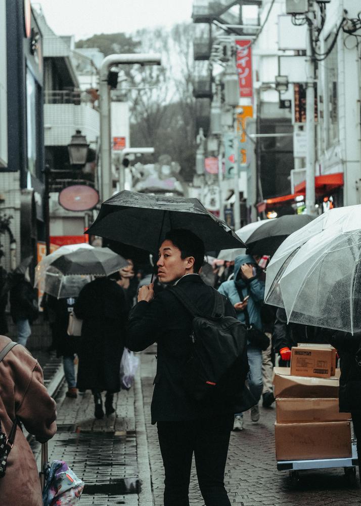 Eine Person mit einem Regenschirm geht durch eine belebte Stadtstraße mit Hochhäusern und Wolkenkratzern.