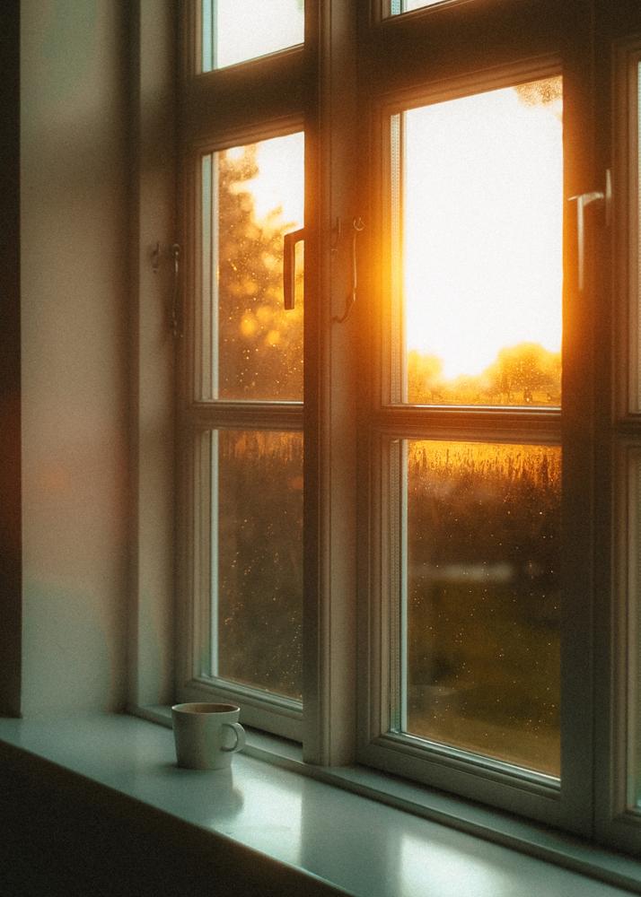 Ein Fenster mit einer Tasse Kaffee auf der Fensterbank, während die Sonne durch die Scheiben scheint.
