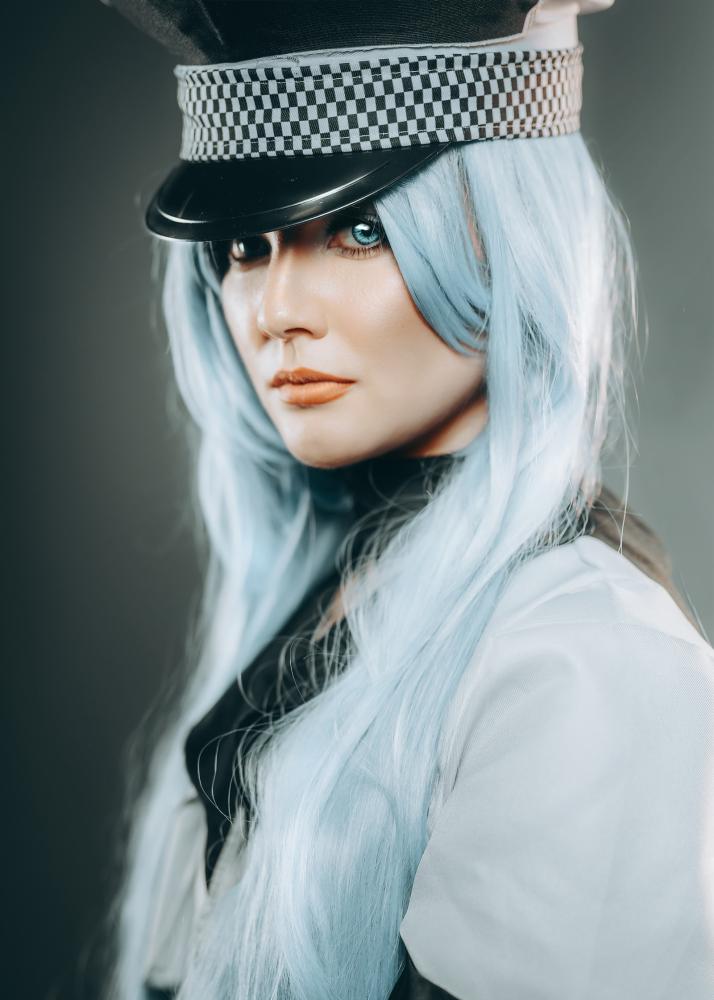 Eine Frau mit blauem Haar, die eine Uniform mit einem Schachbrettmuster-Hut trägt.