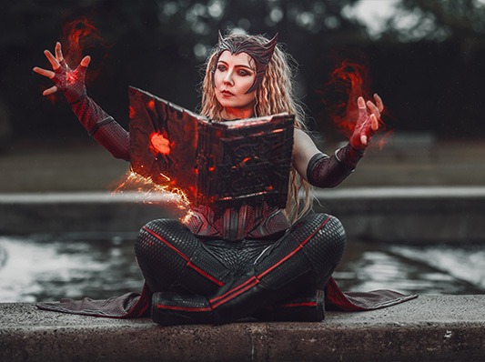 Eine Frau mit rotem Haar und einem futuristischen Kostüm, die ein leuchtendes Buch auf magische Art und Weise hält, während sie auf einem Felsen sitzt.