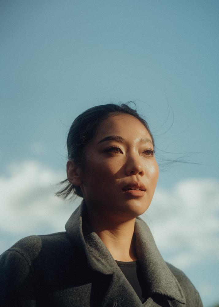 Eine Frau mit glatter Haut und einem leichten Lächeln, die in die Kamera blickt, mit einem klaren Himmel im Hintergrund.
