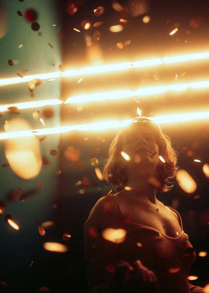 Eine Frau mit geschlossenen Augen, umgeben von fallendem Konfetti und Lichtern.