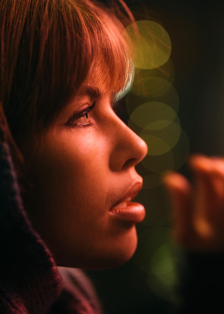 Eine Frau mit einem Pony, die in die Ferne blickt, mit Lichtreflexen auf ihrem Gesicht.