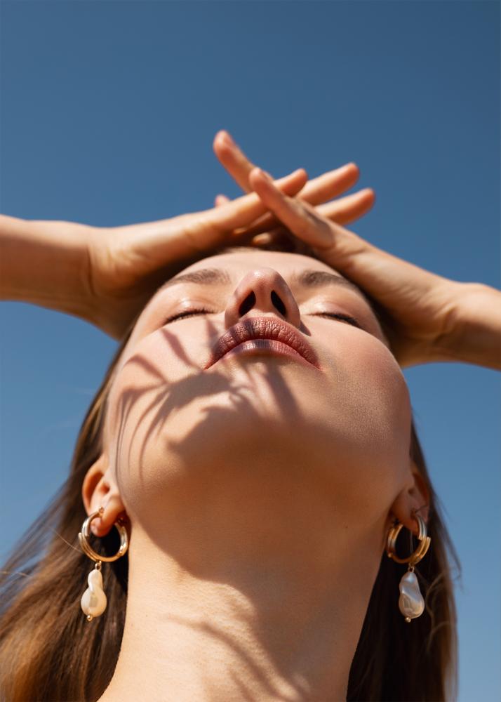 Eine Frau mit geschlossenen Augen und einem glücklichen Lächeln, die ihre Hände über dem Kopf hält, mit Ohrringen in Form von Perlen.