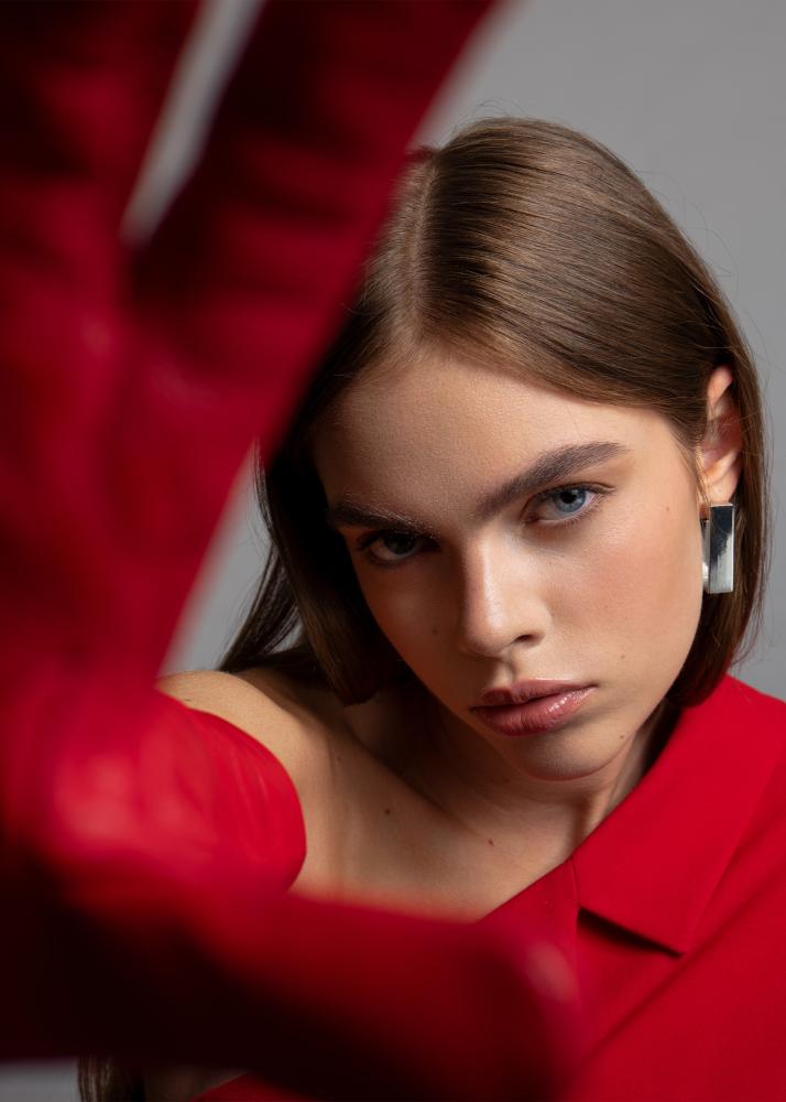 Eine Frau in einem roten Blazer, die ihren Arm in Richtung der Kamera streckt, mit dramatischer Beleuchtung.