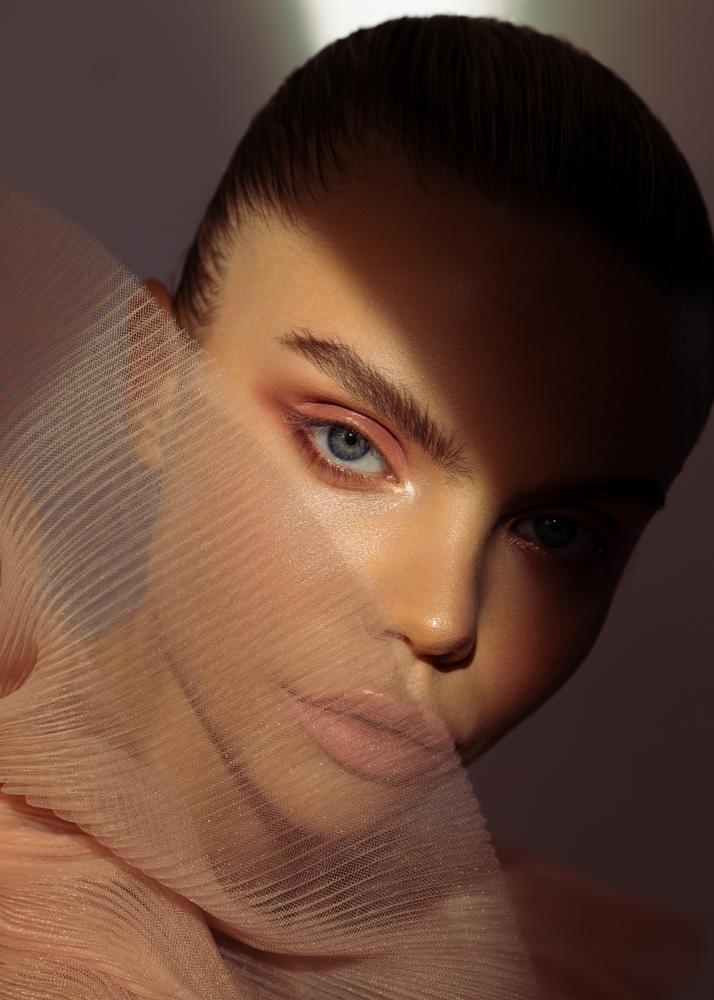 Ein Porträt einer Frau mit einem durchsichtigen Tüllstoff vor dem Gesicht, der seine Augen betont.