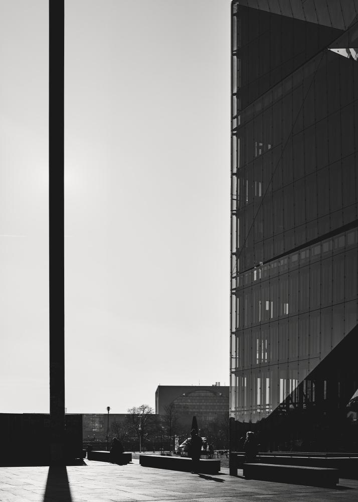 Ein modernes Gebäude mit Glasfassade und Schattenwurf, der geometrische Muster auf dem Boden erzeugt.