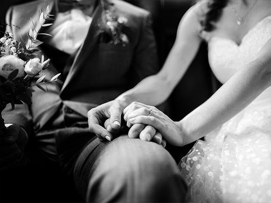 Ein Brautpaar, das sich die Hände hält, während sie in einem Auto sitzen, bereit für ihre Hochzeitsfeier.