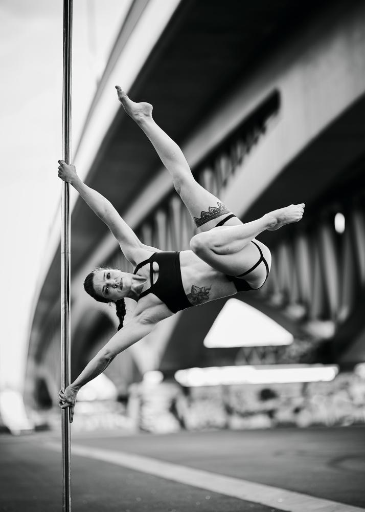 Eine Pole-Tänzerin in einem urbanen Umfeld, die eine beeindruckende Pose auf einem Pfosten einnimmt.