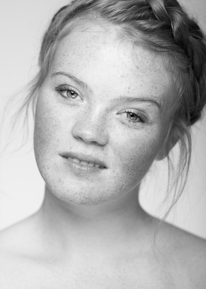 Eine junge Frau mit Sommersprossen im Gesicht und geflochtenem Haar, die direkt in die Kamera blickt.