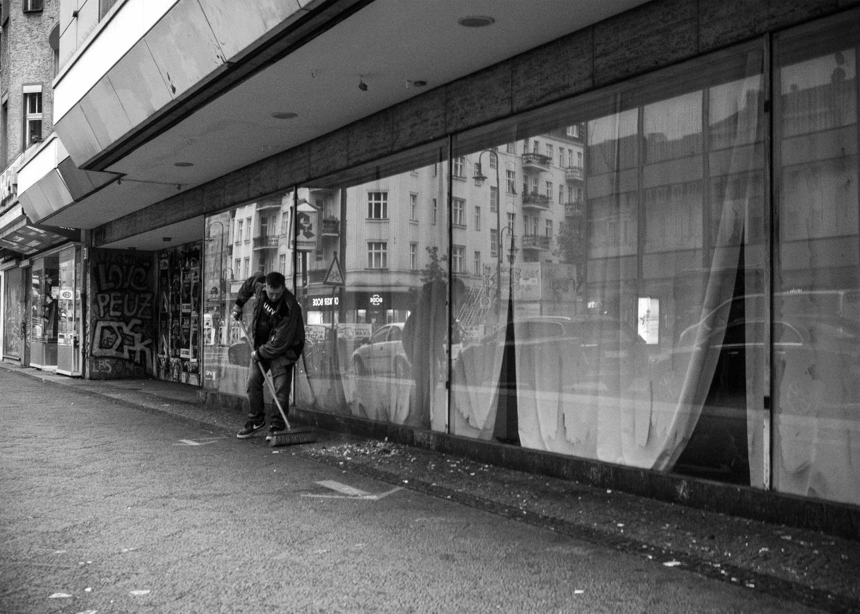 Ein Mann kehrt die Straße vor verhangenen Schaufenstern.