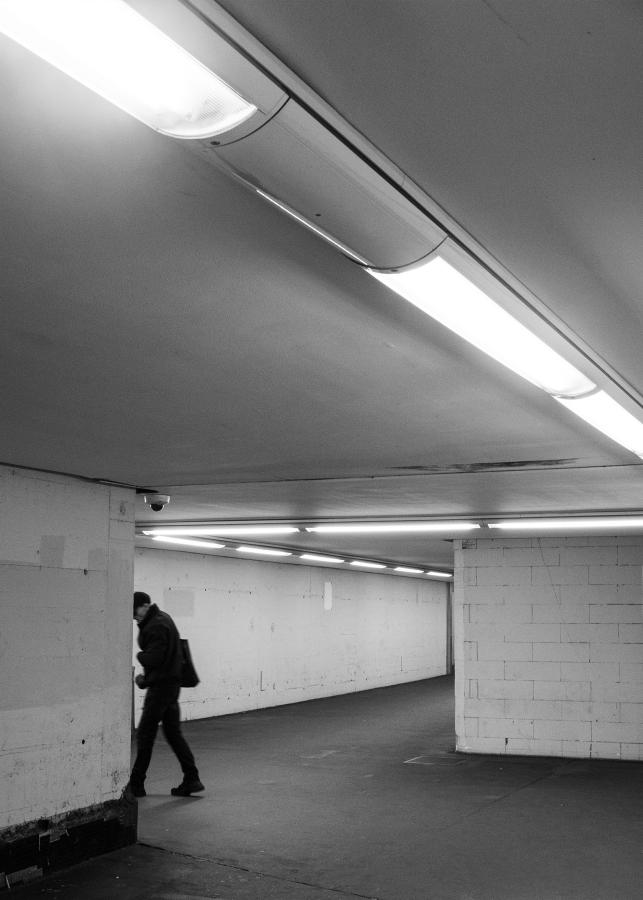 Ein dunkel gekleideter Mann läuft durch die weißen, kargen Wände eines U-Bahnhofes.